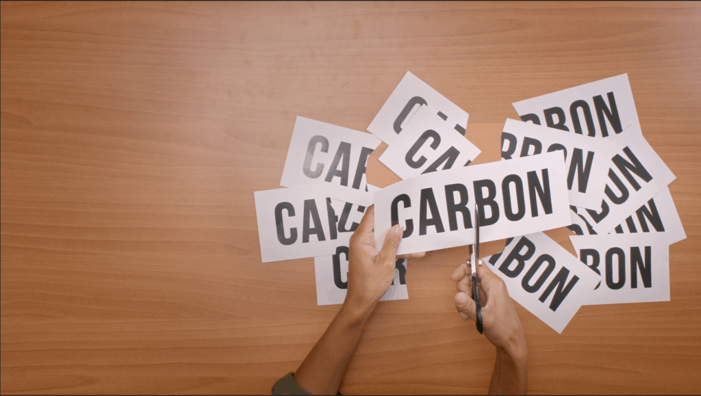 hand with scissors, cutting pieces of paper that say carbon