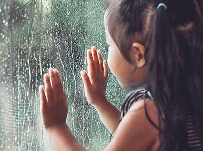child looking at rain through window