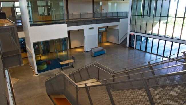 Inside a building lobby with wood trim accents and a blue staircase leading upstairs past a large reception desk