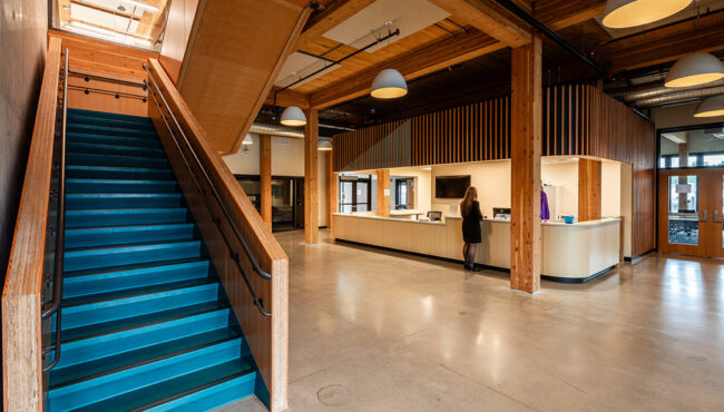 Inside the PCC Metro Opportunity Center lobby with wood trim accents and a blue staircase leading upstairs past a large reception desk