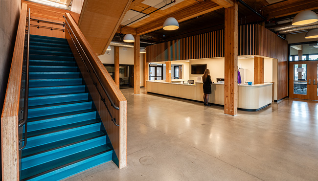 Inside the PCC Metro Opportunity Center lobby with wood trim accents and a blue staircase leading upstairs past a large reception desk