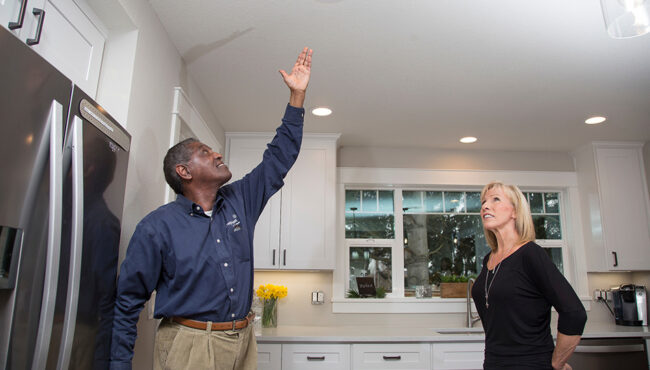 Two people standing in a modern kitchen and one gesturing to the ceiling light