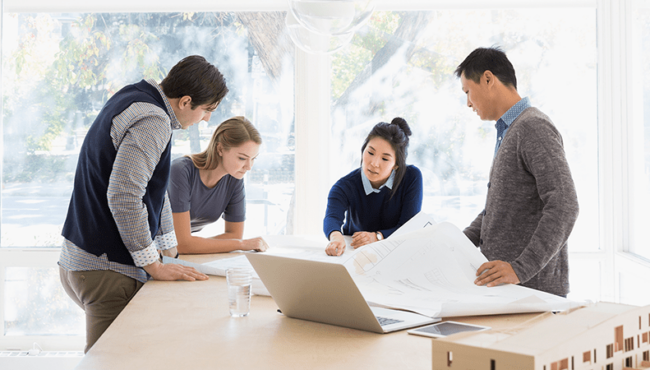 Several people in a bright room looking at a large building plan together.